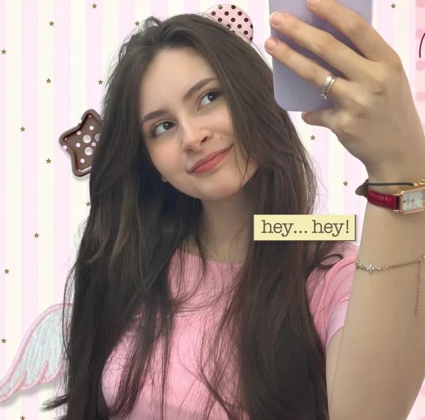 Letícia Laguna sorrindo enquanto tira uma selfie, de blusa rosa, com colagem de estrelas e asas ao fundo